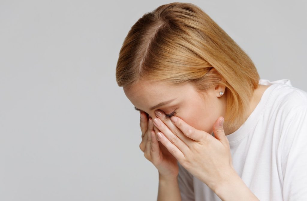 A woman slightly bent over holding her sore dry eyes needing treatment like LipiFlow to provide relief
