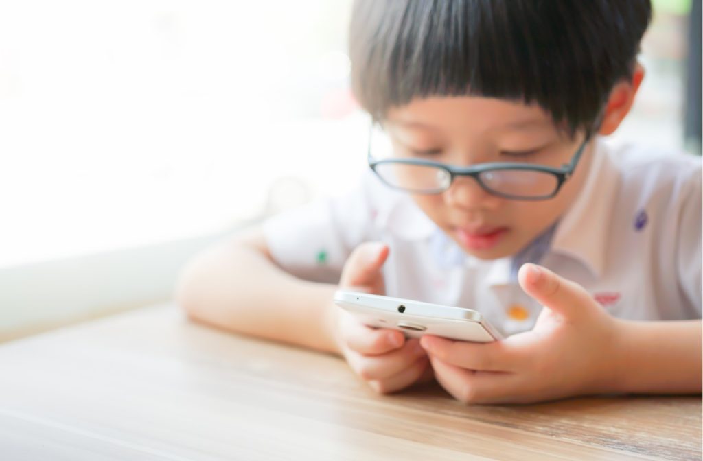 A child with glasses looking closely at a smartphone at a desk